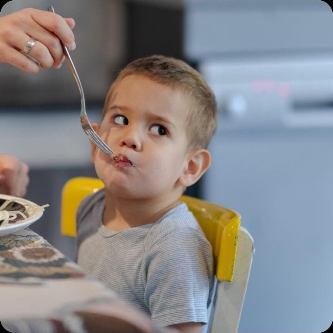 Maminka podává chlapci u stolu sousto na vidličce