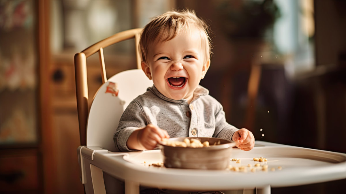 Veselé dítě samo jí jídlo lžičkou. Portrét šťastného chlapečka na vysoké židličce.